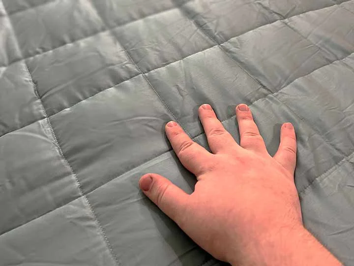 A hand runs over the top of the YnM weighted blanket.