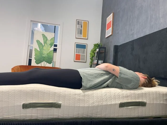 A woman sits on the edge of the Avocado Eco Organic mattress