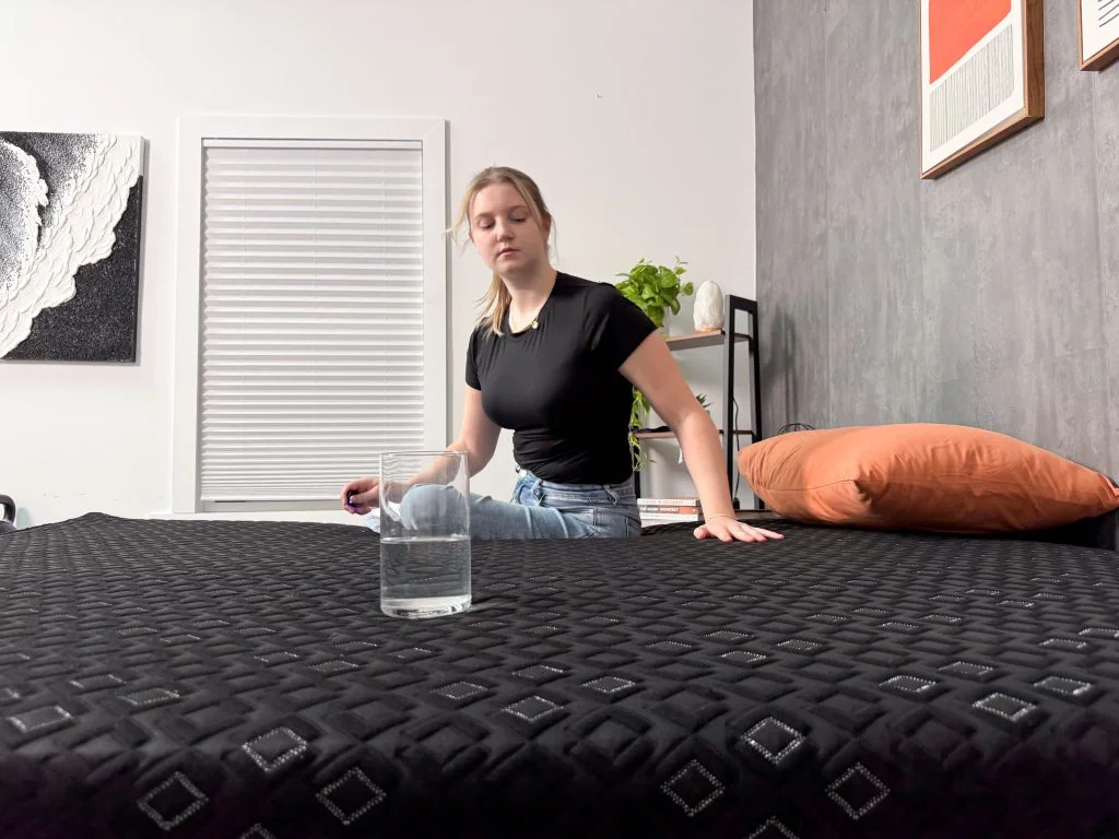 A glass of water sits on one side of the Beautyrest Black Hybrid XCS while our tester moves around on the other