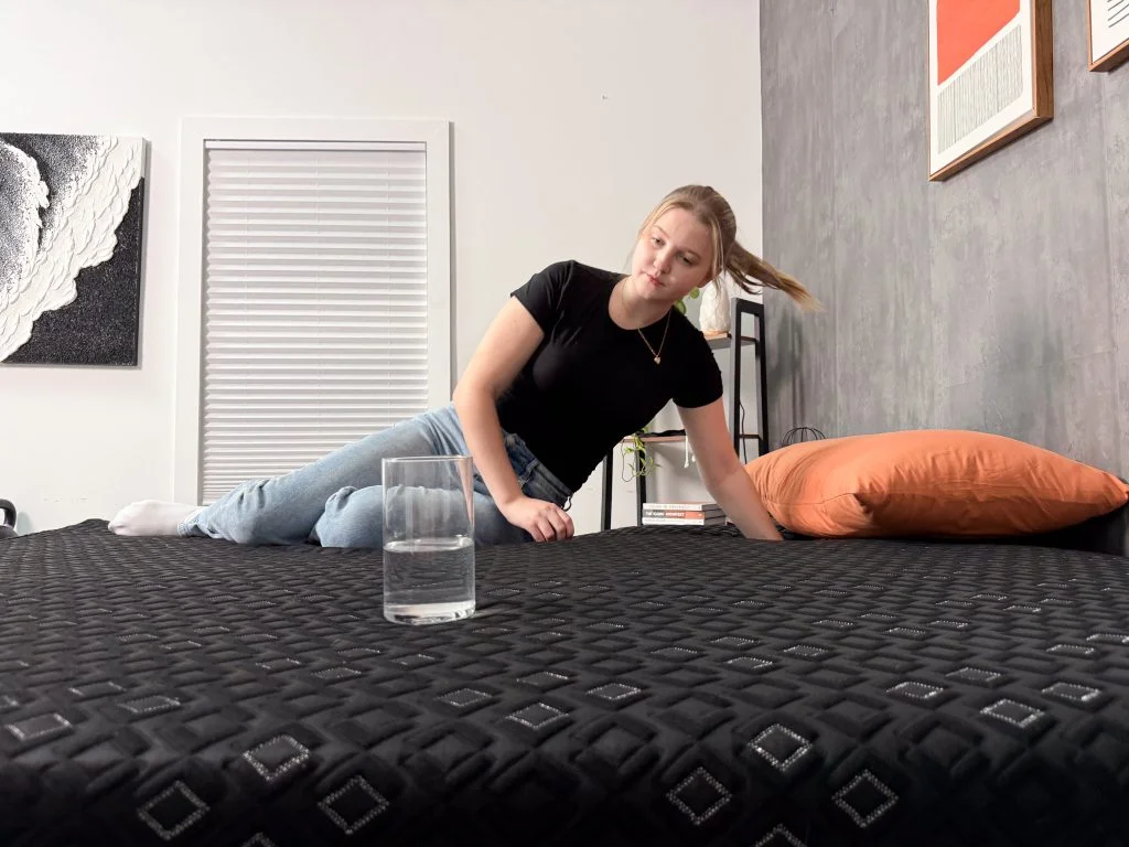 A glass of water sits on one side of the Beautyrest Black Hybrid XCS while our tester moves around on the other