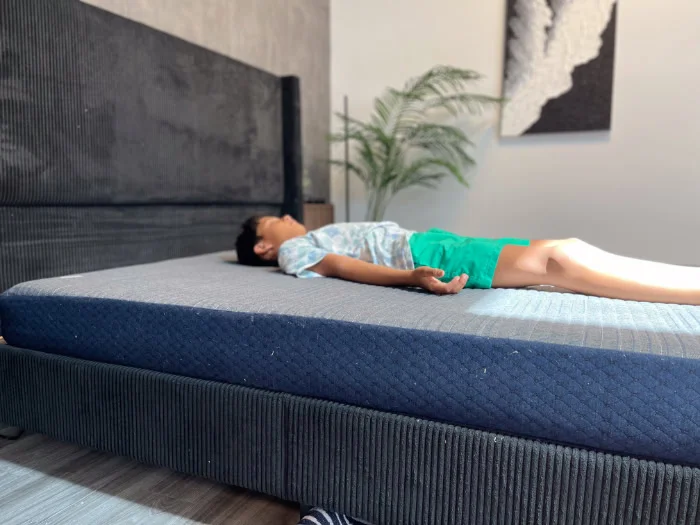 A young boy in a blue shirt and green shorts rests on his back on the Brooklyn Bedding Kids mattress