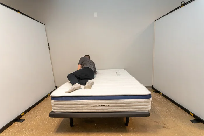 A man moves around near a glass of water to test motion isolation on the Helix Midnight mattress