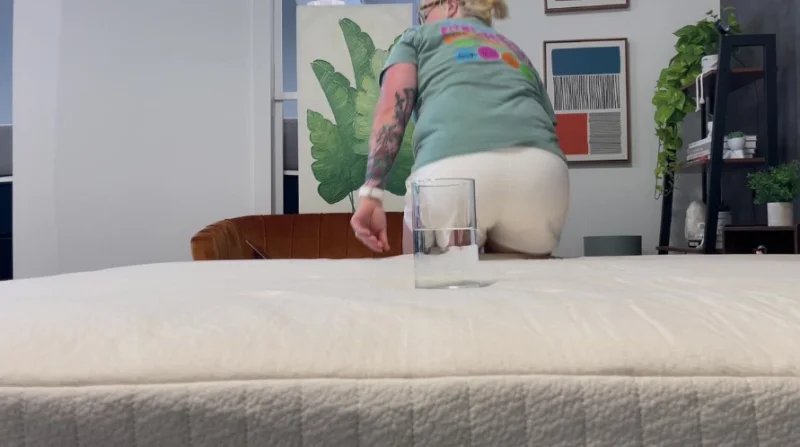 Our tester evaluates the Avocado Eco Organic bed's motion isolation in our water glass test