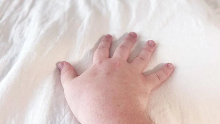 Saatva Linen Sheets Feel An image of a hand brushing across the Saatva linen top sheet.