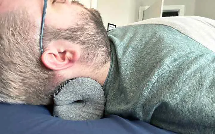 A close up of a man resting his head and neck on the NekGenic Neck Pillow.
