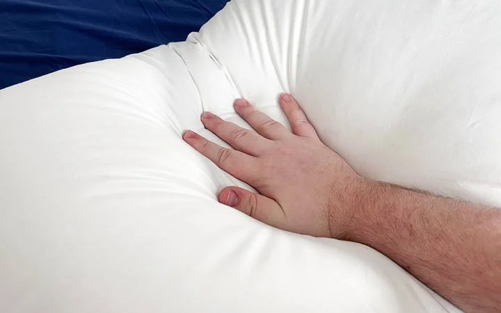 A hand presses into the Plushbeds White Goose Down Pillow. A hand presses into the Plushbeds White Goose Down Pillow.