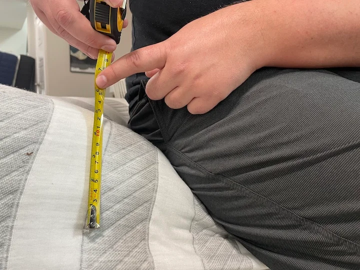 a man measures how much the Leesa Original Mattress sinks when he sits on the side of it