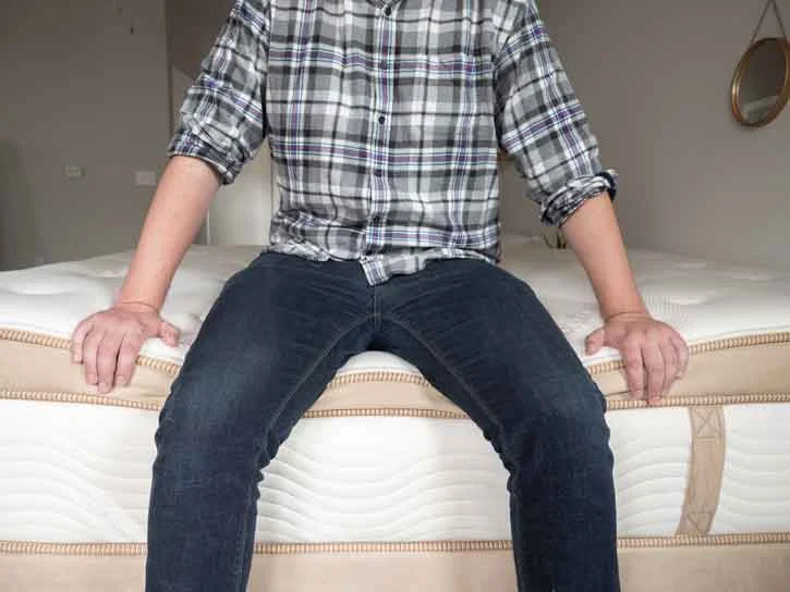 A man sits on the edge of a mattress.