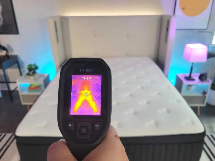 An image of a man pointing a temperature gun at the Titan Plus Luxe mattress. The screen on the temperature gun reads "76.6ºF"