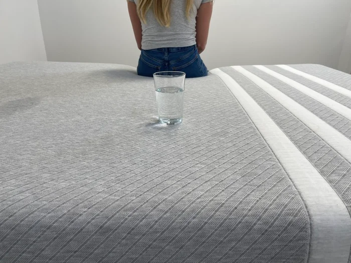 Testing motion isolation on the Leesa Original mattress by sitting on the bed near a glass of water
