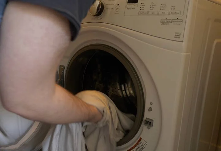 Puffy Bamboo Sheets - A man is putting the sheets into a washing machine. Puffy Bamboo Sheets - A man is putting the sheets into a washing machine.