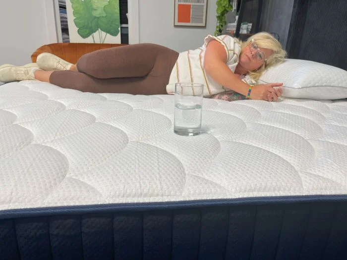 A woman tests motion isolation on the DreamCloud Memory Foam mattress with a glass of water