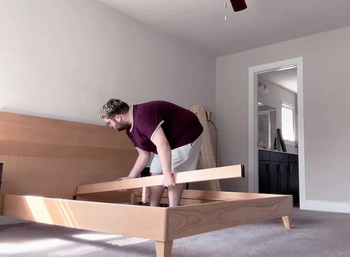 An image of a man setting the middle support piece into the Avocado City Bed Frame